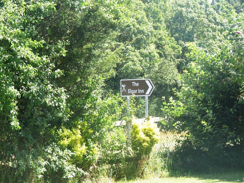 A signpost to the pub next door, under its former name The Elgar Inn, among the hedgerow trees.
